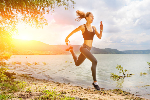 eine schöne sportliche Frau, die in Sportbekleidung am Ufer eines Sees läuft. Mädchen übt - Foto, Bild