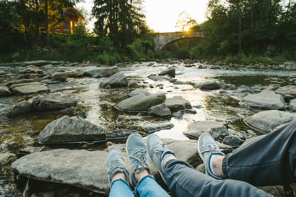 pareja se sienta cerca de río de montaña y mirando al atardecer
 - Foto, Imagen
