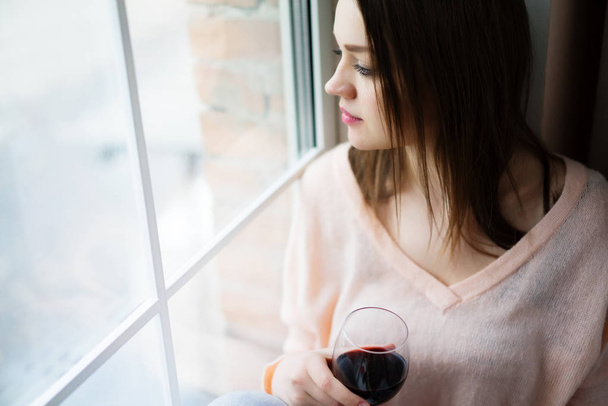 Young woman sitting at window drinking wine - Photo, Image