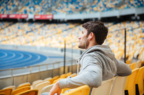 Side view of young man in sportswear with earphones sitting - Фото, зображення