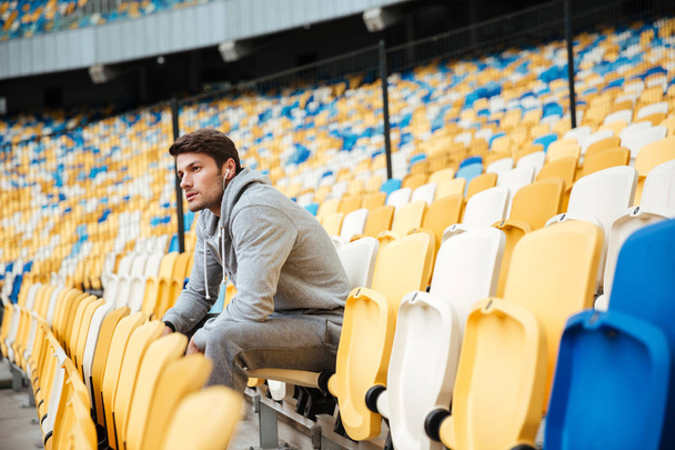 Serious young sports man at the stadium outdoors listening music - 写真・画像