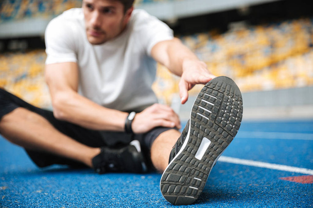 Young sports man at the stadium make stretching exercises. - Foto, Imagen