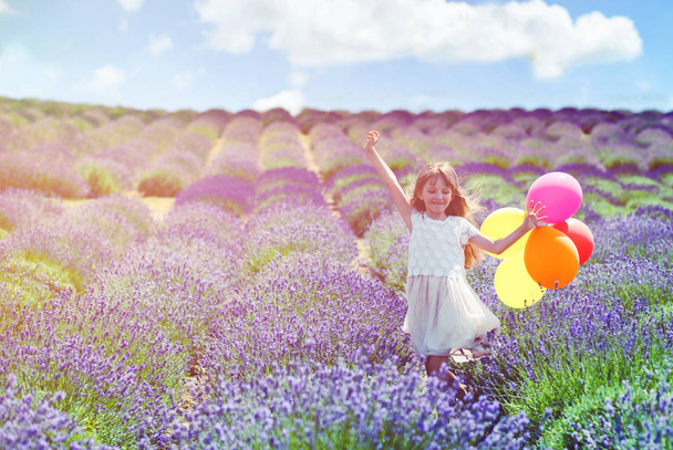 Pretty child girl runs with colorful balloons in lavender field summer freedom concept - Fotó, kép