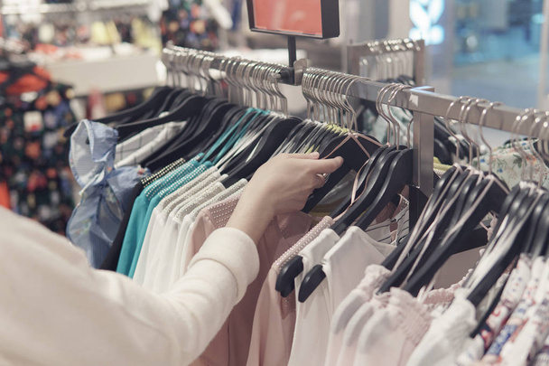 Γυναικεία χέρια, περιφέρεται στα ρούχα σε ένα κατάστημα από δεύτερο χέρι - Φωτογραφία, εικόνα