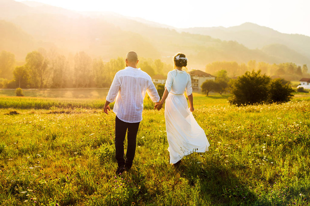 Casal caminhando no campo com vista para o pôr do sol
 - Foto, Imagem