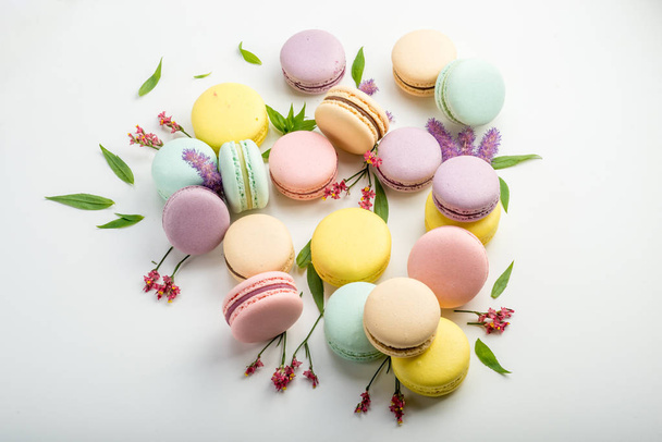 Macarons colorés avec des feuilles et des fleurs rouges sur un fond blanc. Dessert délicat français
 - Photo, image