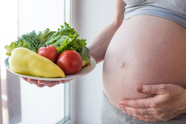 Беременная женщина, держащая тарелку с овощами. Концепция контроля веса и здорового питания во время беременности
 - Фото, изображение