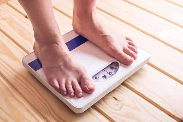 Female feet standing on mechanical scales for weight control on wooden background. Concept of slimming and weight loss - Photo, Image