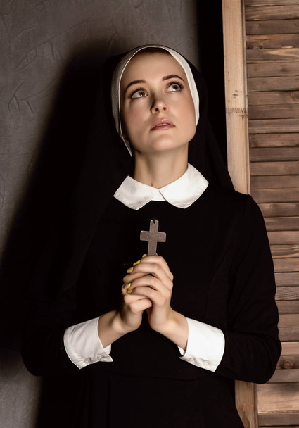 Humble young beautiful nun in robes holding a cross on a grey background - Photo, Image