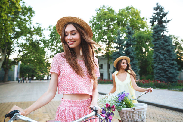 Kaksi nuorta onnellista naista seisoo ulkona polkupyörien kanssa
 - Valokuva, kuva