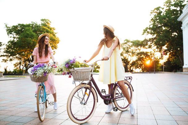 Two young pretty women in dresses sitting on retro bicycles - Foto, afbeelding