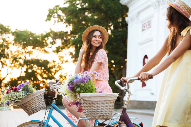 Due donne sorridenti felici in cappelli che cavalcano biciclette vintage
 - Foto, immagini