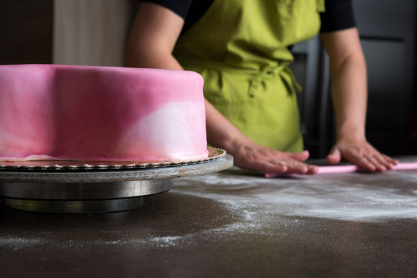 Unrecognisable woman preparing pink fondant for cake decorating, focus on the cake - 写真・画像