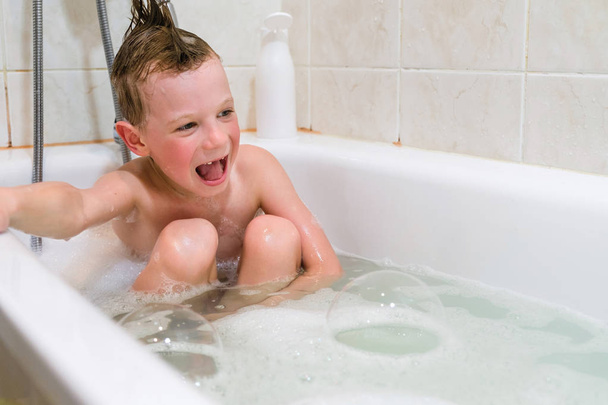 a child plays in a bathtub with soap bubbles at home - Fotó, kép