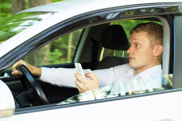 Νεαρός άνδρας χρησιμοποιεί το τηλέφωνο πίσω από το τιμόνι ενός αυτοκινήτου - Φωτογραφία, εικόνα