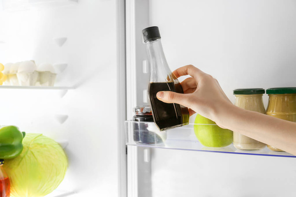Hand of young woman taking bottle with soy sauce from fridge - Fotó, kép