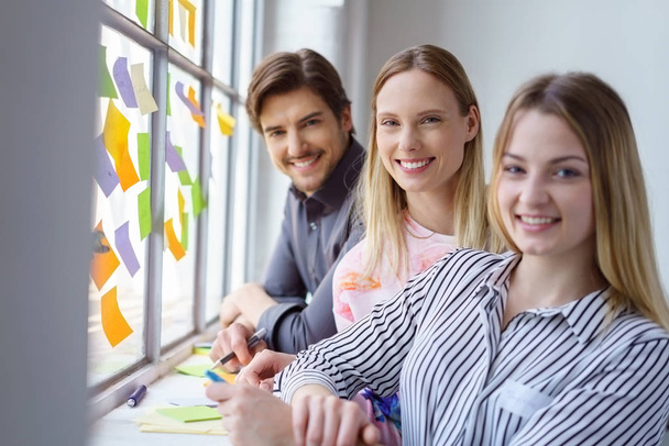 Two women and man standing near window with colorful sticky notes in office - Valokuva, kuva