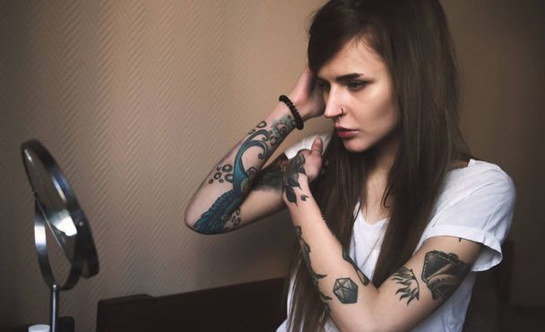 Jovem mulher tatuada fazendo maquiagem na frente do espelho
 - Foto, Imagem