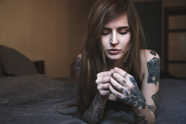 Young tattooed woman with long hair lying on the bed - Fotoğraf, Görsel