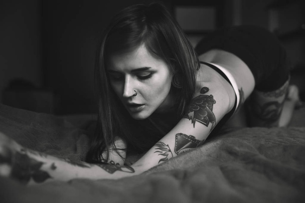 Τατουάζ γυναίκα με μακριά μαλλιά πόζες στο κρεβάτι - Φωτογραφία, εικόνα