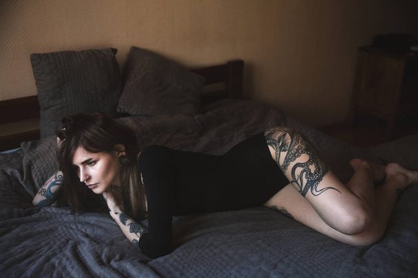 Young tattooed woman with long hair pose in the bedroom - Photo, Image