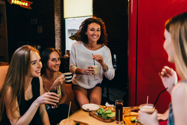 Четыре веселые подружки веселятся, болтают, смеются, едят и пьют в ресторане быстрого питания
 - Фото, изображение