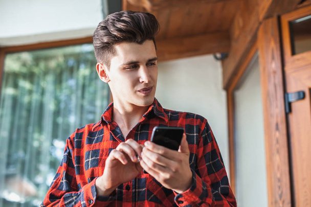 Stylish handsome young man with a serious expression holding a smart phone in hand and looking at him. The concept of communication, correspondence and contemporary works - Foto, Bild