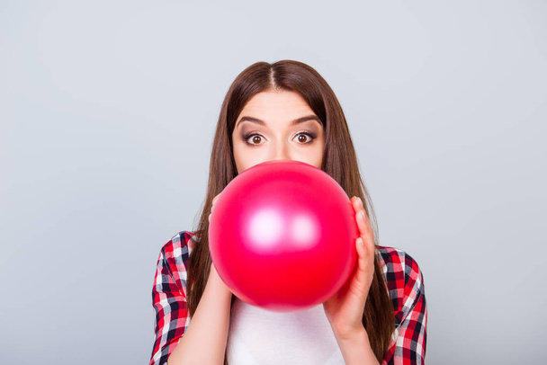 Young amazed brown-haired girl is blowing red balloon for birthd - Foto, afbeelding