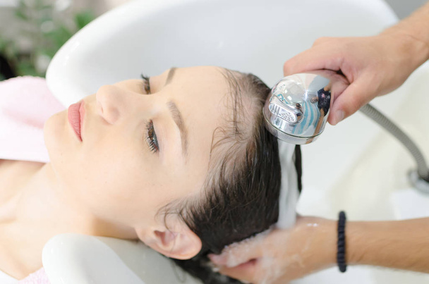 Hairdresser rinse woman hair and head in hair beauty salon after balm for healthy hair care. - Fotó, kép