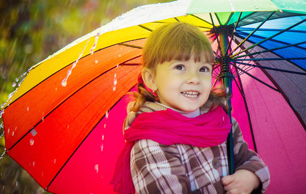 Dziecko jest w deszczu. Z parasolem. Selektywny fokus.  - Zdjęcie, obraz