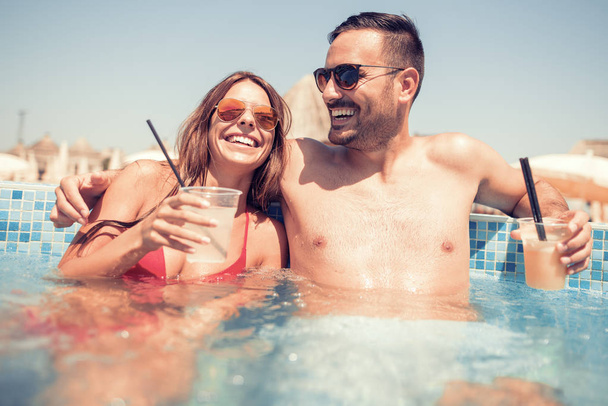 Beautiful couple drinking cocktails in the swimming pool - Photo, Image