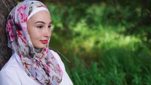 Portrait of a thoughtful and slightly cunning Muslim woman who sits near a tree - Footage, Video