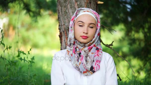 Portrait of a brooding and young Muslim woman, who sits in a forest near a tree - Footage, Video