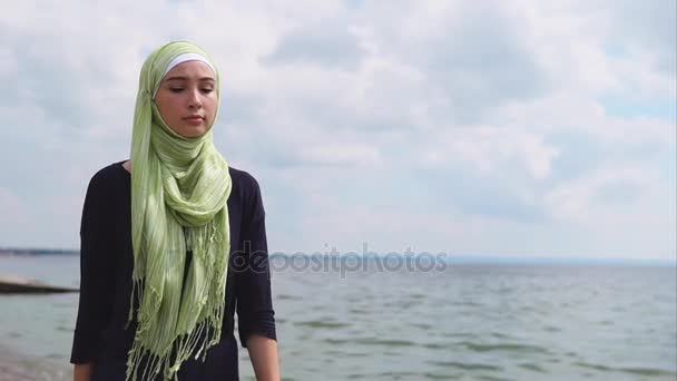 Μια νεαρή μουσουλμάνα σε ένα πέπλο έρχεται με μια σκεπτικός ματιά κατά μήκος της θάλασσας - Πλάνα, βίντεο