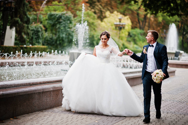 Wedding couple walking and smiling on pavement with a fountain i - Fotó, kép