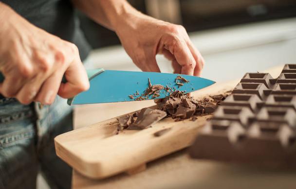 Woman hands chopping chocolate block for celebratory cake - Foto, afbeelding