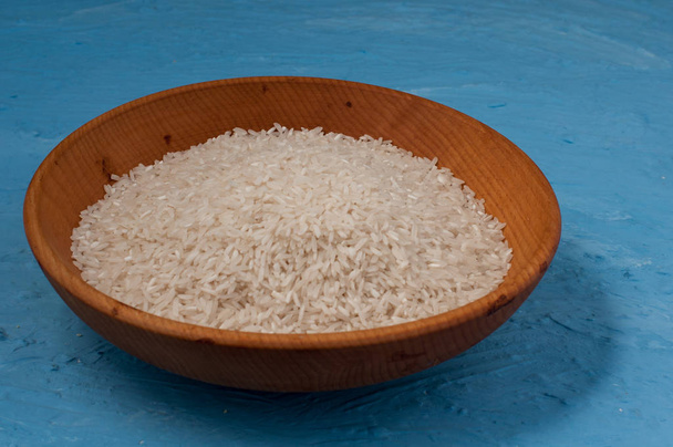 witte rijst in houten kom op blauwe achtergrond - Foto, afbeelding