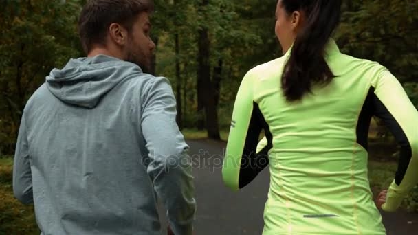 Vrouw en man communiceren en glimlachen tijdens ochtend joggen. Ze draaien op het park. - Video