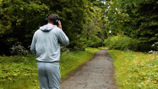 Mężczyzna runner w ciepłe ubrania w jesienny park, słuchanie muzyki i kaptur ubrania. - Materiał filmowy, wideo