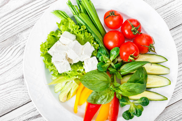 Assiette de légumes frais avec fromage feta, tomates cerises, concombre, céleri, poivron et basilic dans une assiette sur fond bois fermer. Vue du dessus
 - Photo, image