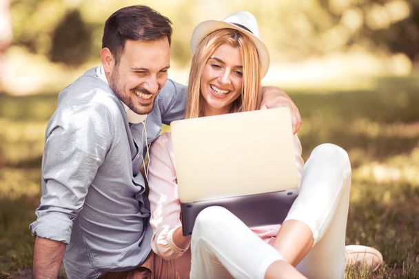 junges Paar sitzt auf Gras und benutzt Laptop im Park. - Foto, Bild