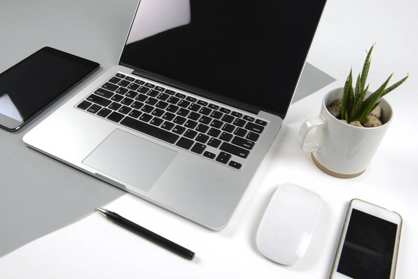 Mesa de oficina con ordenador portátil, portátil, tableta digital y smartphone en un moderno fondo bicolor (blanco y gris)
. - Foto, imagen
