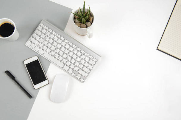 Office table with  keyboard, mouse, notebook and smartphone on modern two tone (white and grey) background. - Фото, изображение