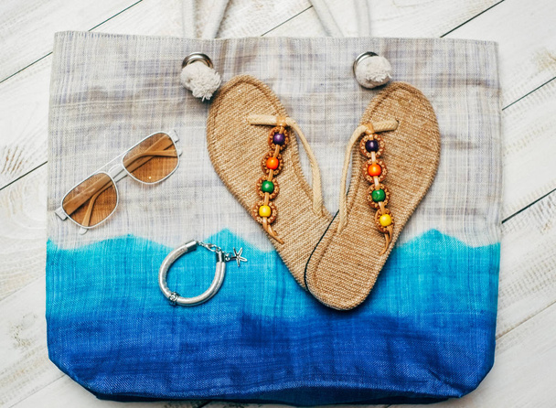  Flat lay of summer fashion with slippers and sunglasses on top of the bag on white wooden background - Valokuva, kuva