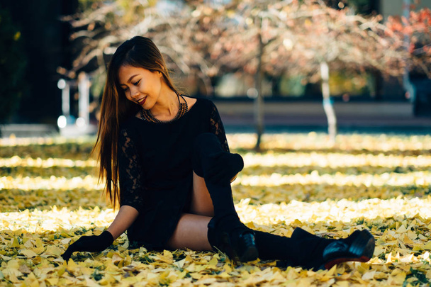  Happy young woman in park on sunny autumn day, laughing, playing leaves. Cheerful beautiful girl in black retro dress autumn fashion style - Fotografie, Obrázek
