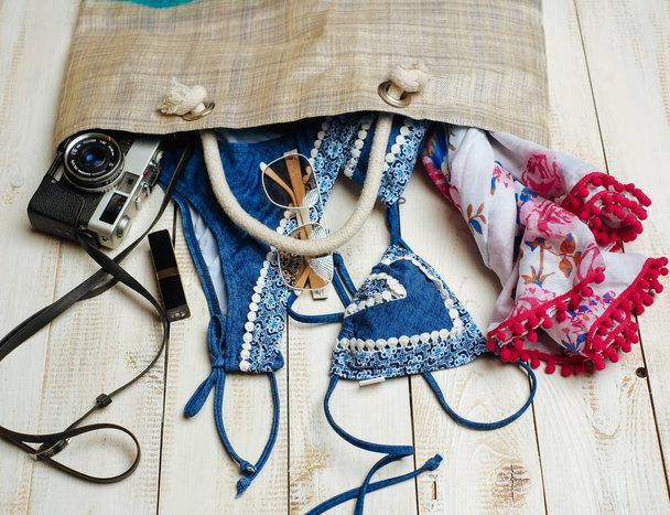  Flat lay of summer fashion with blue bikini swimsuit inside the bag, and other girl accessories on white wooden  background - 写真・画像