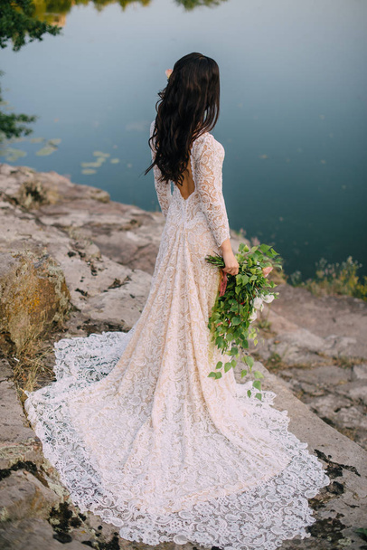 Young bride standing on rocky river bank, sunset - 写真・画像