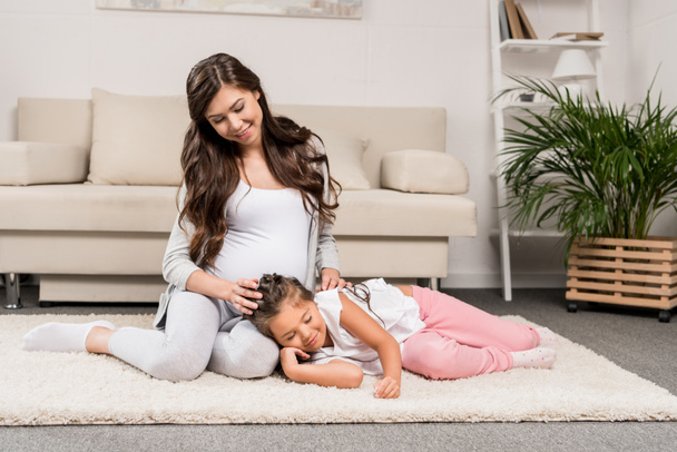 Pregnant woman with daughter sitting on rug  - Фото, зображення