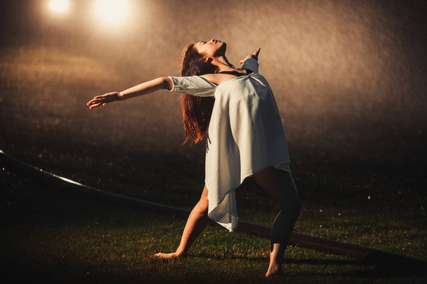 Ballerina staat op gazon in avond naast spray uit sprinklin - Foto, afbeelding