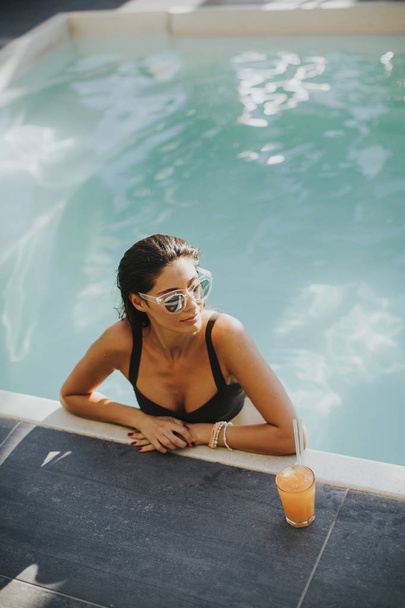 Mulher jovem junto à piscina com coquetel
 - Foto, Imagem